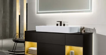 Un meuble sous plan Finion avec des compartiments à étagères éclairés Un lavabo Finion avec meuble sous plan éclairé et miroir lumineux dans une salle de bains sombre.