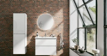 Une salle de bains loft moderne avec des collections de salle de bains de Villeroy & Boch, un mur de briques, une grande fenêtre, un lavabo blanc avec un miroir rond, un tapis et une plante en pot.