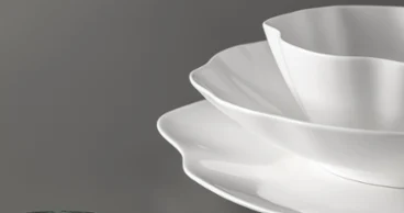 Trois assiettes blanches Pura à bord dentelé sont posées sur une surface grise. Trois assiettes blanches Pura à bord dentelé sont empilées sur une surface grise à côté d'un objet rond vert.