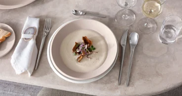 Des assiettes et des couverts de table de Villeroy & Boch avec du potage à la crème Une table dressée avec des assiettes et des couverts de table NewMoon de Villeroy & Boch, avec un potage à la crème servi.