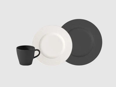 Image de la collection - Manufacture Une tasse noire, une assiette blanche et une assiette noire sont disposées ensemble sur un fond sobre gris clair.