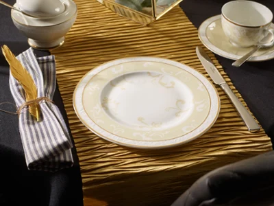 Ivoire sur une table Un couvert avec assiette, couteau, fourchette, tasse, sous-tasse et serviette sur un chemin de table à la structure dorée.