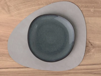 Une assiette Lave est posée sur un set de table Lifestyle Accessories gris sur une table en bois. Une assiette Lave est posée sur un set de table Lifestyle Accessories gris sur une table en bois.
