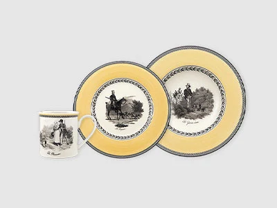 Image de la collection - Audun Une tasse et deux assiettes avec un bord jaune et des illustrations noires de scènes pastorales sur fond gris clair.