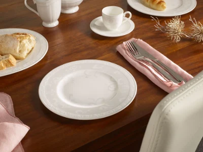 Vaisselle Gray Pearl sur une table Assiette blanche, couverts sur une serviette rose, tasse et pâtisserie sur une table en bois dressée pour un repas.