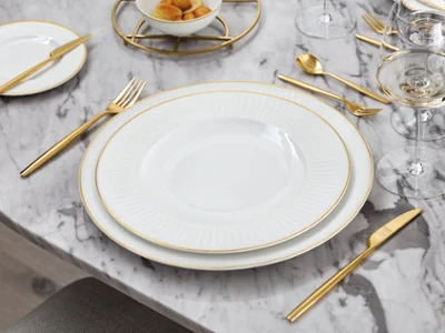 La collection Château Septfontaines dressée sur une table en marbre Un ensemble de vaisselle blanc et doré de Château Septfontaines sur une table en marbre.
