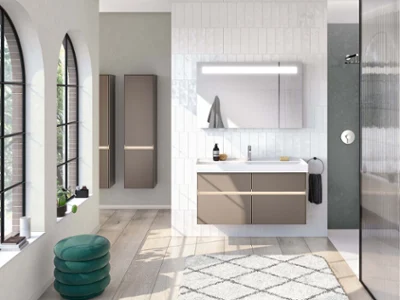 Des meubles de salle de bains Collaro dans une salle de bains lumineuse Un intérieur de salle de bain moderne avec des placards Collaro blanc et beige, un grand miroir More to See, une douche à l’italienne et des fenêtres cintrées offrant une vue sur la verdure