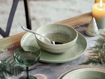 Un bol Perlemor vert avec une cuillère repose sur une assiette assortie Un bol Perlemor vert avec une cuillère repose sur une assiette assortie, posée sur une table avec des bougies et des décorations végétales