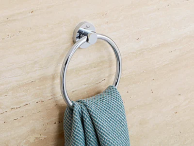Un anneau porte-serviettes Elements Tender avec une serviette bleue Sur un mur en marbre beige est fixé un anneau chromé sur lequel est posé une serviette bleue structurée.