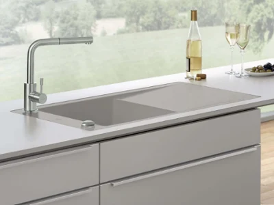 Un évier de cuisine gris Timeline 60 flat à fleur de plan avec une robinetterie dans une cuisine lumineuse avec deux verres à vin, une bouteille de vin et des olives dans une coupe.