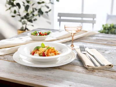 Une assiette de pâtes New Cottage sur une table en bois. Une assiette de pâtes avec des légumes et des herbes, une salade et une boisson sur une table en bois dressée pour une personne.