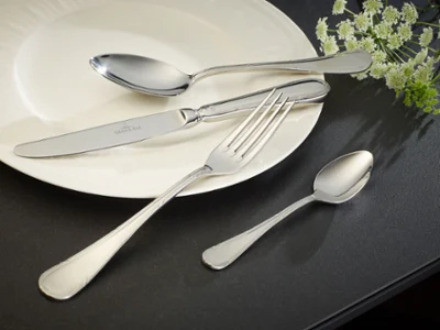 Une assiette blanche avec des couverts de table de la collection Kreuzband Septfontaine Une assiette blanche avec des couverts de table de la collection Kreuzband Septfontaine sur une surface noire.