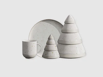 Image de la collection - Winter Glow Un ensemble de vaisselle en céramique blanche, dont une tasse, une assiette et des bols empilables en forme d'arbre, sur un fond sobre.