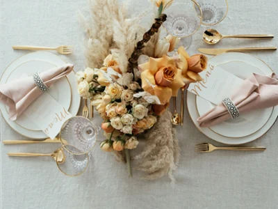 Une table élégamment dressée avec de la vaisselle dorée et des couverts de table MetroChic de style bohème Une décoration de table élégante avec des couverts de table MetroChic dorés, de la vaisselle Anmut avec un bord doré, un centre de table floral et des menus.
