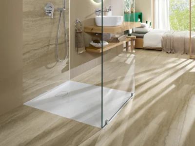 Receveur de douche Ecora dans une douche à l'italienne ouverte à côté d'une chambre Receveur de douche Villeroy & Boch Ecora dans une douche à l'italienne ouverte avec des surfaces aspect travertin, à côté d'une chambre lumineuse avec vue sur le jardin.