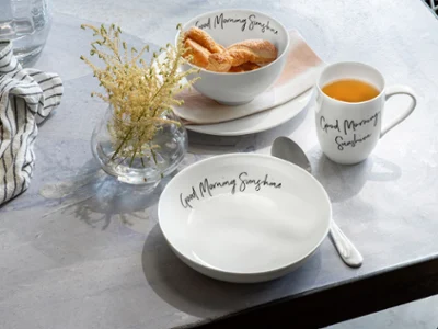 Une tasse Statement, une assiette et bol « Good Morning Sunshine » sur une table Une table avec une tasse à café Statement et une assiette Statement de Villeroy & Boch contenant des croissants.