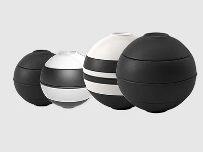 Image de la collection - La Boule & La petite Boule Quatre objets sphériques noirs et blancs avec des bandes horizontales, disposés en ligne sur un fond gris clair.