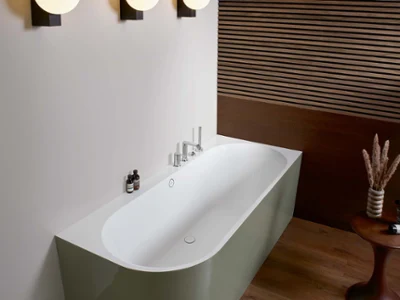 Oberon 2.1 ovale. Une baignoire blanche à l’intérieur, un habillage vert à l’extérieur Une salle de bains moderne avec une baignoire en îlot, trois appliques murales rondes, du lambris en bois et une petite table d’appoint avec des objets décoratifs.