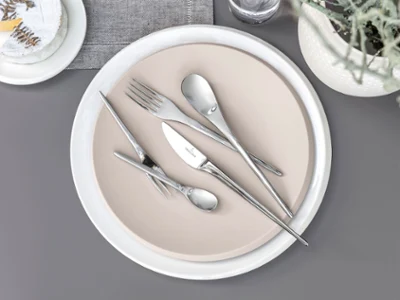 Des couverts de table NewMoon sur une assiette beige Des couverts de table NewMoon de Villeroy & Boch disposés sur une assiette beige placée sur un fond gris.