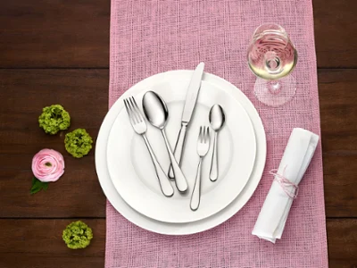 Sur une table soigneusement arrangée, on peut voir la collection Oscar de Villeroy & Boch. Sur une table soigneusement arrangée, on peut voir la collection Oscar de Villeroy & Boch. Une assiette blanche est complétée par d’élégants couverts de table argentés et un verre à vin, le tout posé sur un set de table rose. À côté, se trouvent une serviette roulée et des fleurs vertes et roses éclatantes.