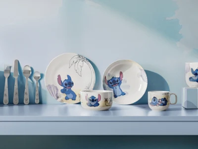 Une série d'assiettes et de tasses de la collection Disney Stitch sont disposées sur une étagère bleu clair. Une série d'assiettes et de tasses de la collection Disney Stitch sont décorées de motifs de dessins animés et exposées sur une étagère bleu clair avec des ustensiles.