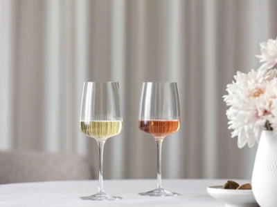 Deux verres à vin Afina de Villeroy & Boch sont posés sur une table à côté d'un vase avec des fleurs roses. Deux verres à vin Afina de Villeroy & Boch, l'un rempli de vin blanc et l'autre de rosé, sont posés sur une table à côté d'un vase avec des fleurs roses.