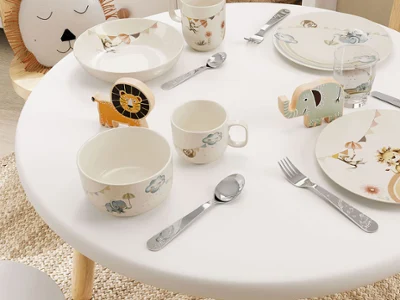 De la vaisselle Boho Kids dressée sur une petite table dans une chambre d’enfant Une table dressée dans une chambre d’enfant avec de la vaisselle Boho-Kids, des couverts de table et des verres sur le thème des animaux dans des couleurs pastel.