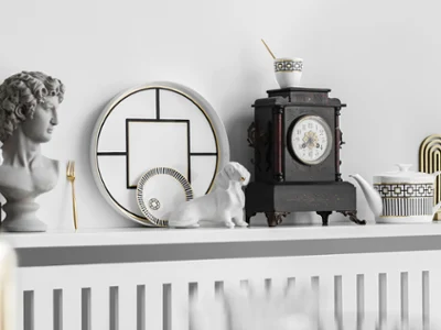 De la vaisselle MetroChic sur une présentation avec de la décoration Sur une étagère, on peut voir un buste, des assiettes décoratives MetroChic, une figurine représentant un teckel, une horloge ouvragée et une théière MetroChic avec une tasse assortie.