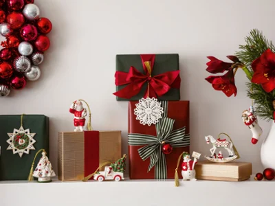 Des ornements Christmas Classic pour une décoration festive Une décoration festive avec des cadeaux emballés, une couronne avec des boules rouges et argentées et des ornements festifs Christmas Classic, disposés de manière ordonnée sur une surface blanche.