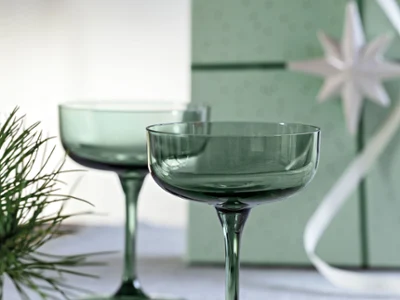 Verre Like Sage idéal comme cadeau Deux verres à cocktail verts sur une surface blanche avec une boîte cadeau verte et des branches de sapin en arrière-plan.