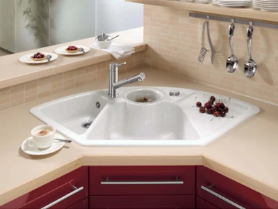 Un coin cuisine moderne avec un évier blanc sur un meuble rouge. Sur le plan de travail, on peut voir des ustensiles, une tasse de café et des aliments.