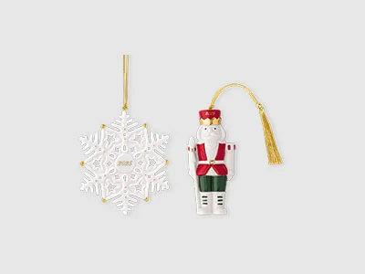 Image de la collection - Christmas Classic Un ornement blanc en forme de flocon de neige et un ornement en forme de casse-noisette avec des cordes suspendues dorées sur un fond sobre.