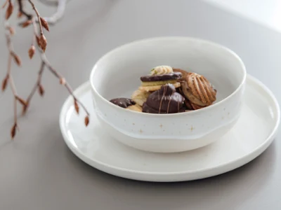 Une assiette et un bol Winter Glow avec des biscuits Un saladier Winter Glow avec différents biscuits sur une assiette Winter Glow et des branches décoratives en arrière-plan.