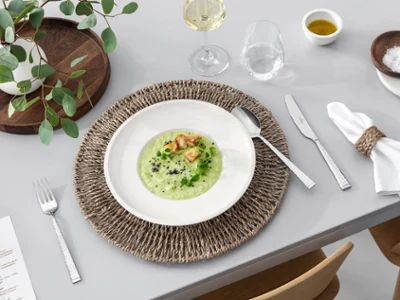Des couverts de table Blacksmith et des assiettes Artesano de Villeroy & Boch, accompagnés d’une décoration rustique et de vin blanc Une table dressée pour le repas avec des couverts de table Blacksmith, une assiette Artesano remplie de soupe, un verre à vin blanc et une décoration de table rustique.