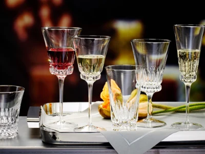 Des verres Grand Royal remplis de vin Une sélection de verres en cristallin Grand Royal de Villeroy & Boch, chacun rempli d’une boisson différente, est artistiquement disposée sur un plateau argenté à côté d’une serviette pliée et d’une tulipe orange.