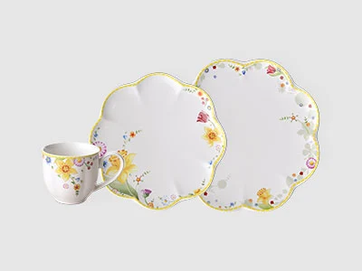 Image de la collection - Spring Awakening Sur un fond sobre, on peut voir une tasse avec un motif floral et deux assiettes assorties avec un bord ondulé et des touches de vert et de jaune.