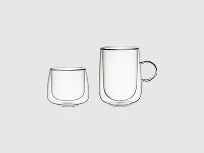 Image de la collection - Verres Artesano Deux gobelets en verre transparent à double paroi, l'un avec anse et l'autre sans, sont représentés sur un fond clair et sobre.