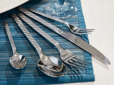 Un ensemble de couverts de table Montauk argentés sur un set de table tissé bleu Un ensemble de couverts de table Montauk argentés disposés sur un set de table tissé bleu à côté d’une assiette blanche et d’un verre.