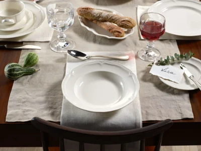 Une table de salle à manger élégamment dressée avec de la vaisselle Manoir Un table de salle à manger avec des assiettes Manoir avec du pain et des citrouilles décoratives sur une table en bois rustique.