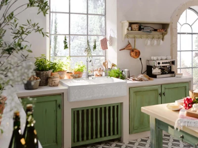Un évier timbre d’office dans une cuisine champêtre avec des portes en bois vert, des ustensiles de cuisine et beaucoup d’épices et d’herbes aromatiques.
