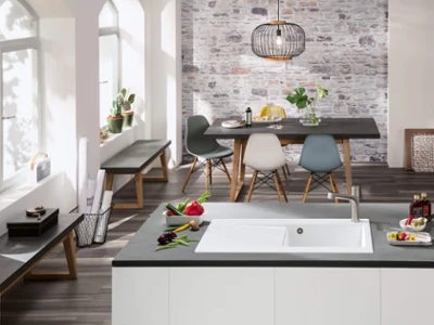 Un intérieur de cuisine moderne avec un plan de travail noir et un coin repas avec des chaises de couleur pastel.