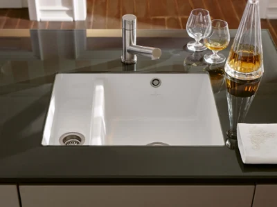 Un évier de cuisine moderne avec un seul robinet, encastré dans un plan de travail noir, avec deux verres.