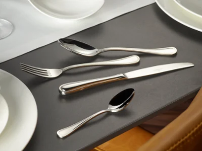 Des couverts de table Merlemont sur une table noire Les couverts de table Merlemont de Villeroy & Boch, composés d’une fourchette, d’un couteau, d’une cuillère à soupe et d’une cuillère à café, sont soigneusement disposés à côté d’assiettes blanches et d’un plat creux sur une table foncée.
