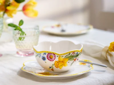La tasse à thé et la soucoupe « Spring Awakening » avec cuillère de Villeroy & Boch. La tasse à thé et la soucoupe « Spring Awakening » avec cuillère de Villeroy & Boch sont posées sur la table, à côté de verres en cristal et de fleurs doucement floues en arrière-plan.