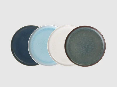 Image de la collection - Crafted Quatre assiettes rondes en céramique de couleur bleu foncé, bleu clair, blanc et vert, disposées côte à côte sur un fond clair.