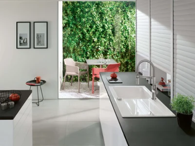 Un évier en céramique Architectura avec une robinetterie de cuisine sur un plan de travail noir avec un ensemble de tables en arrière-plan