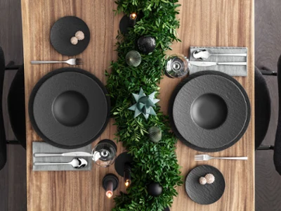 Une élégante table de fête avec des assiettes noires Manufacture Une élégante table de fête avec des assiettes noires Manufacture, des couverts de table et des décorations de fête vert foncé sur une table en bois.