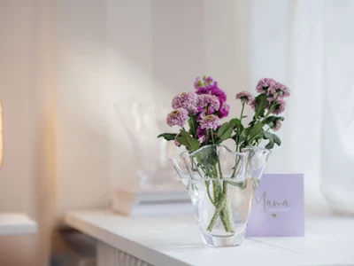 Un vase Blossom avec des fleurs violettes sur une table Un vase Blossom avec des fleurs violettes sur une table, à côté d’une carte portant l’inscription « Mama » (Maman).