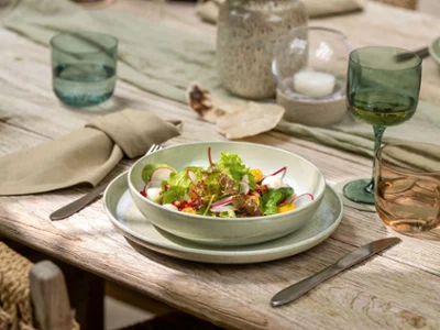 Un saladier Perlemor trône sur une table dressée Un saladier trône sur une table dressée avec des verres, des assiettes et des serviettes beiges Perlemor.