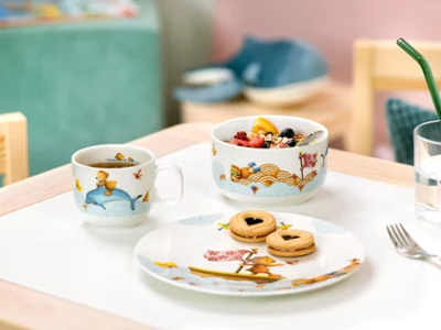 Un ensemble pour le petit-déjeuner Kiddy Bears avec un petit-déjeuner sur une table Un ensemble pour le petit-déjeuner Kiddy Bears avec une tasse décorée, une coupe à fruits et une assiette de biscuits sur une table.